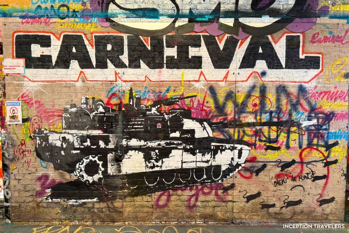 Stencilled tank mural under the word Carnival, surrounded by tags and painted rats in Leake Street