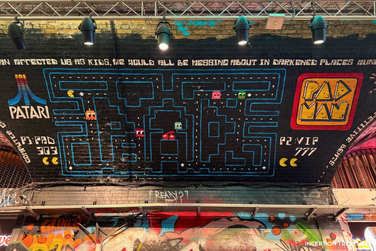 Pac-Man maze mural with ghosts and a Patari logo painted across a black railway arch in Leake Street