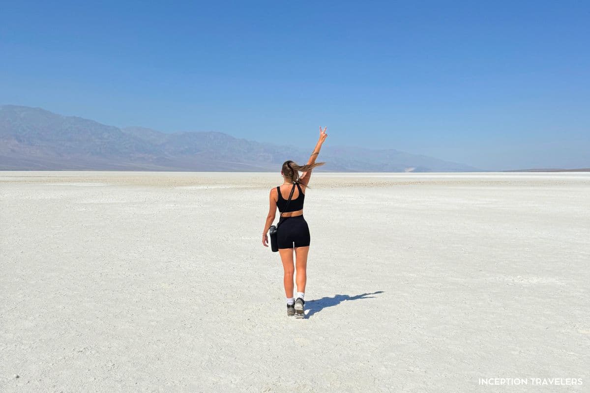 Traveler raising a peace sign while walking across the white salt flats of Badwater Basin in Death Valley