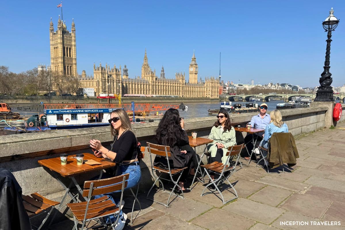 Customers at folding tables along the Thames embankment, Victoria Tower and Big Ben across the river