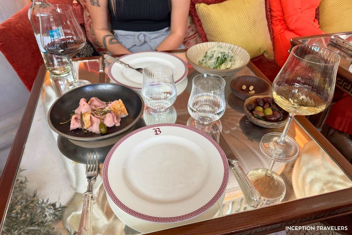 Starters, olives and white wine on a mirrored Bacchanalia table set with Greek-key rimmed plates