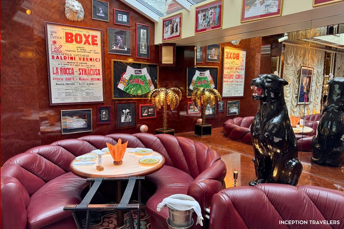 Curved burgundy leather booths beneath vintage Italian boxing posters, gold palm lamps and a black panther statue