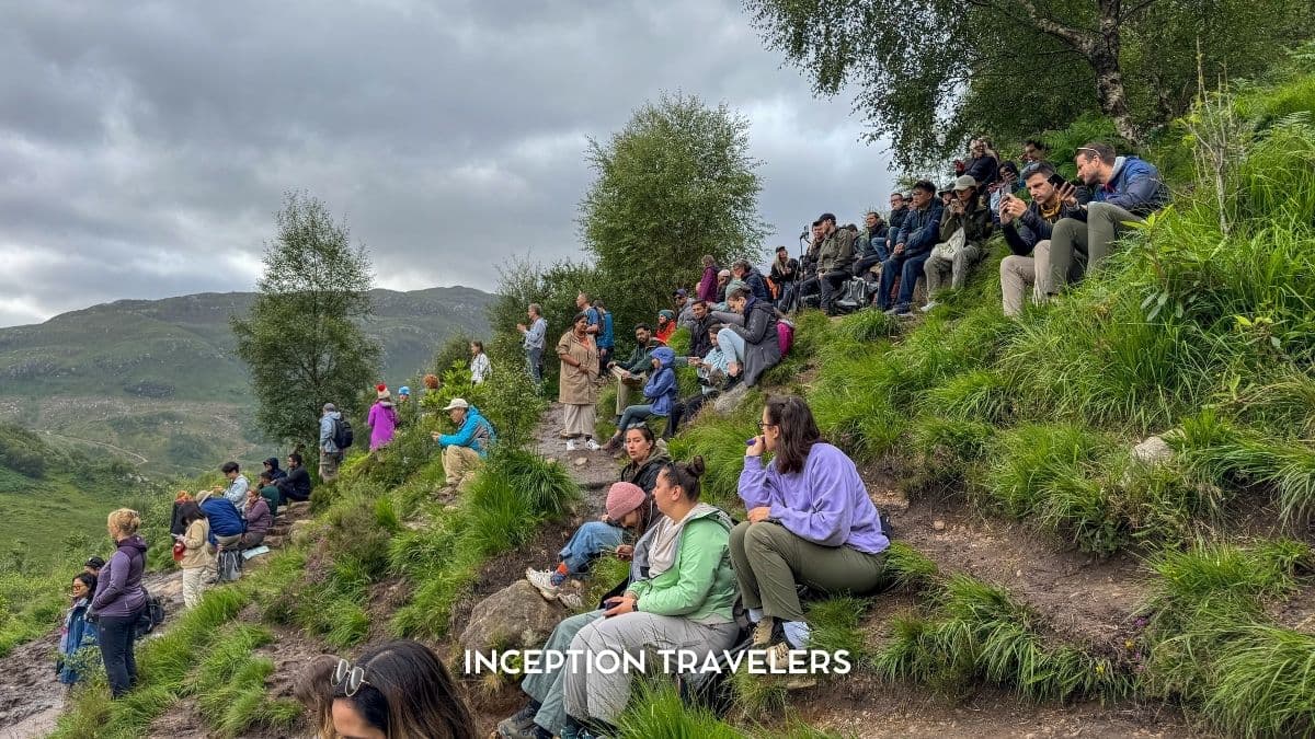 People gathered on a grassy hillside in the Scottish Highlands, waiting and watching for a steam train to pass