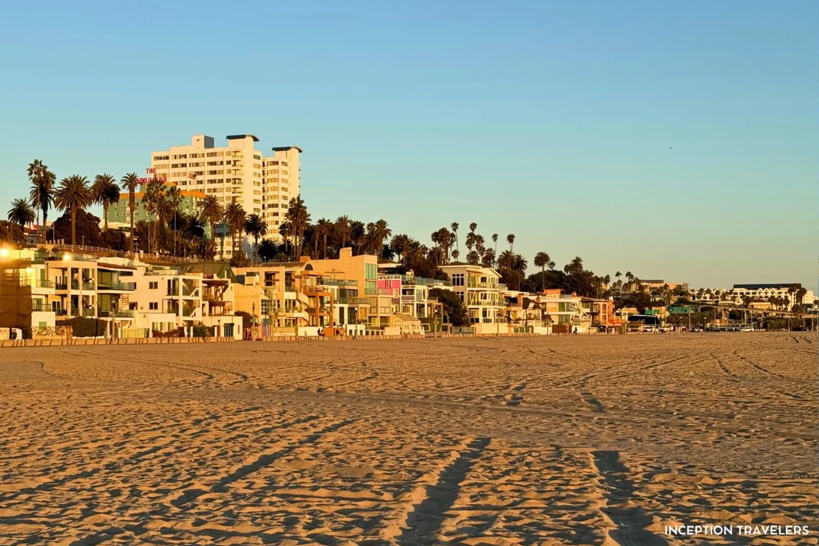 Beach houses and palm trees along the sand of Santa Monica State Beach at golden hour