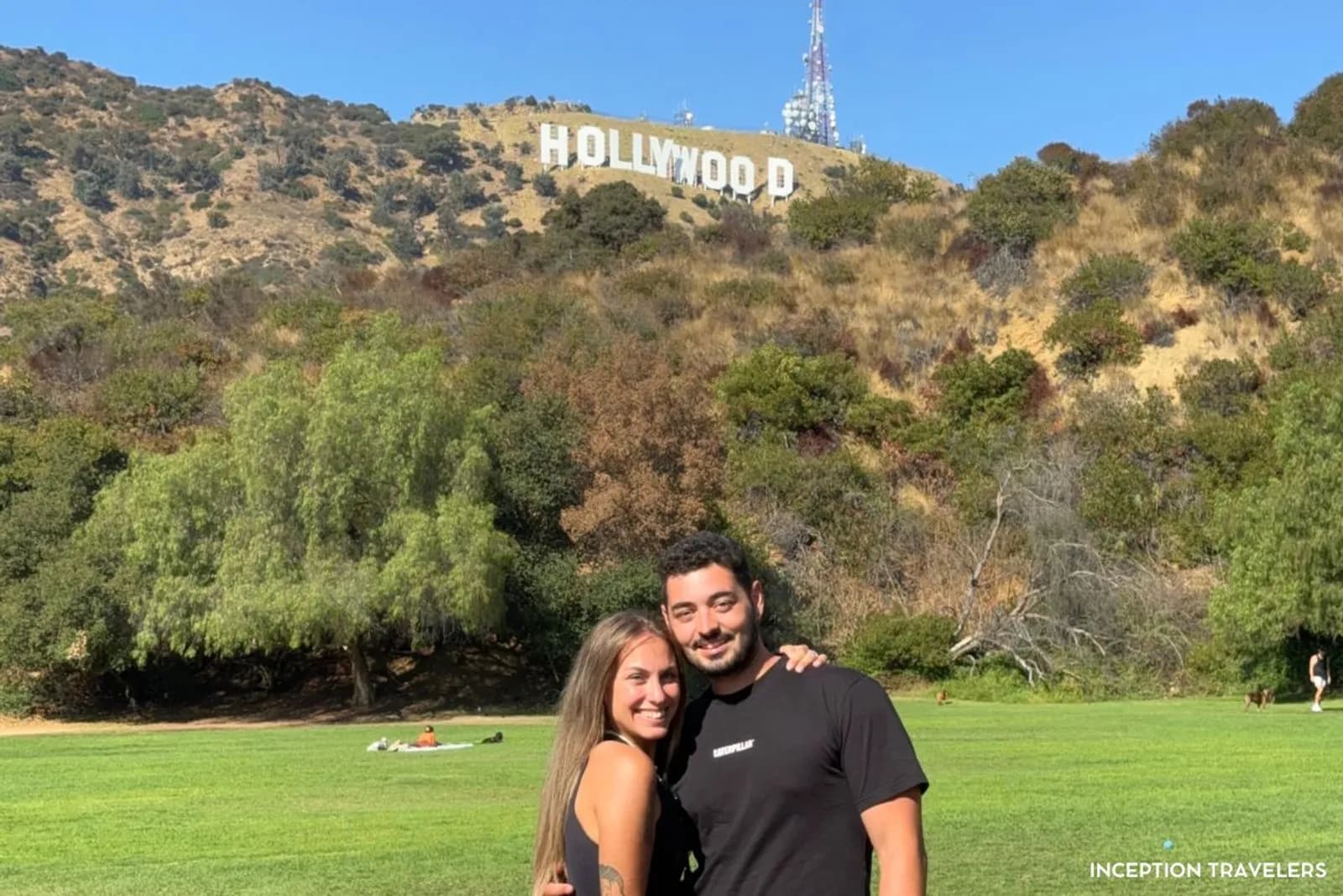 Couple posing on the grass of Lake Hollywood Park with the Hollywood Sign on the hill behind