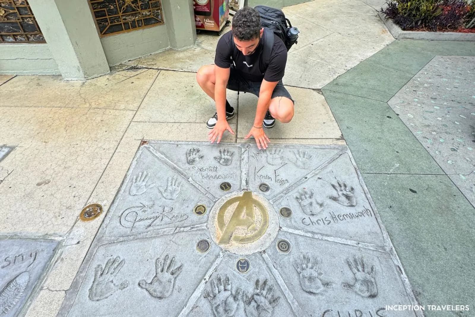 Man crouching over the Avengers cast handprints in the forecourt of the TCL Chinese Theatre