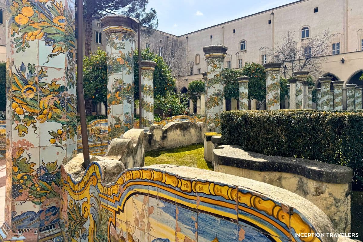 Hand-painted majolica columns and tiled benches in the sunlit garden of the Santa Chiara cloister
