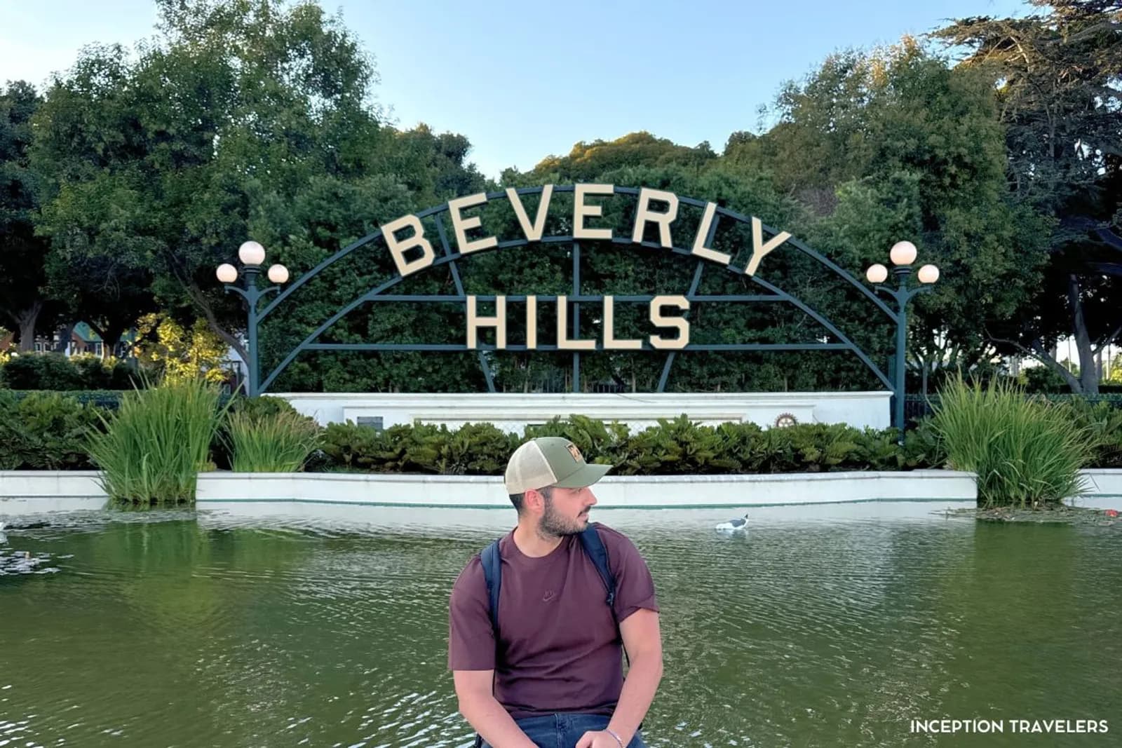 Man in a cap sitting at the lily pond in front of the arched Beverly Hills garden sign